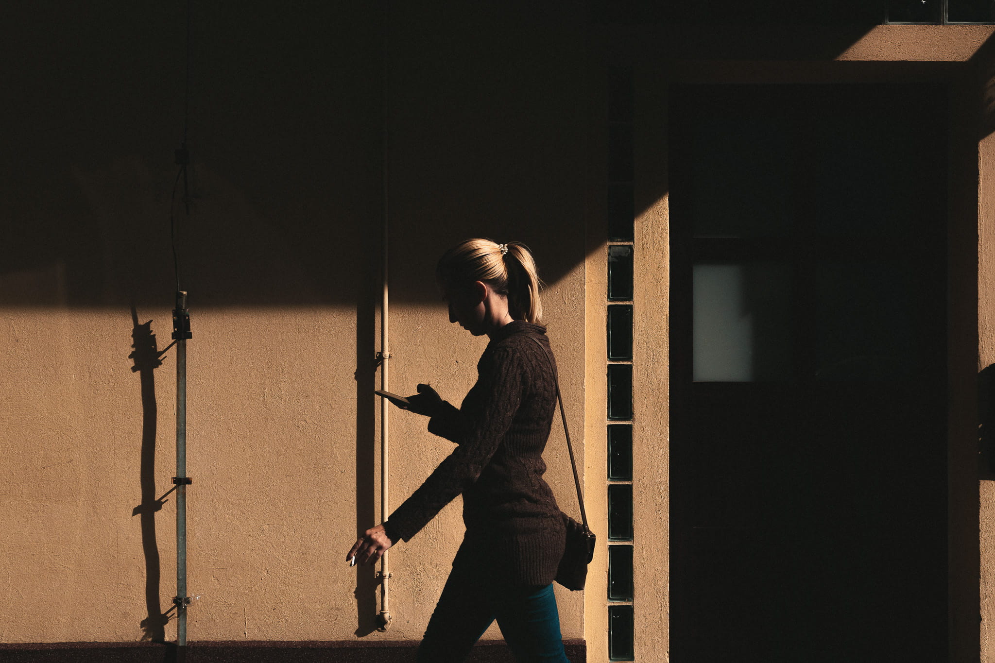 Blonde lady in a suit walking infront of a wall looking down at her phone in her hand