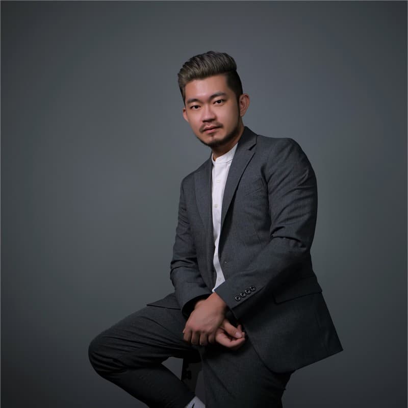 A professional portrait of a man in a grey suit and white shirt against a plain grey background
